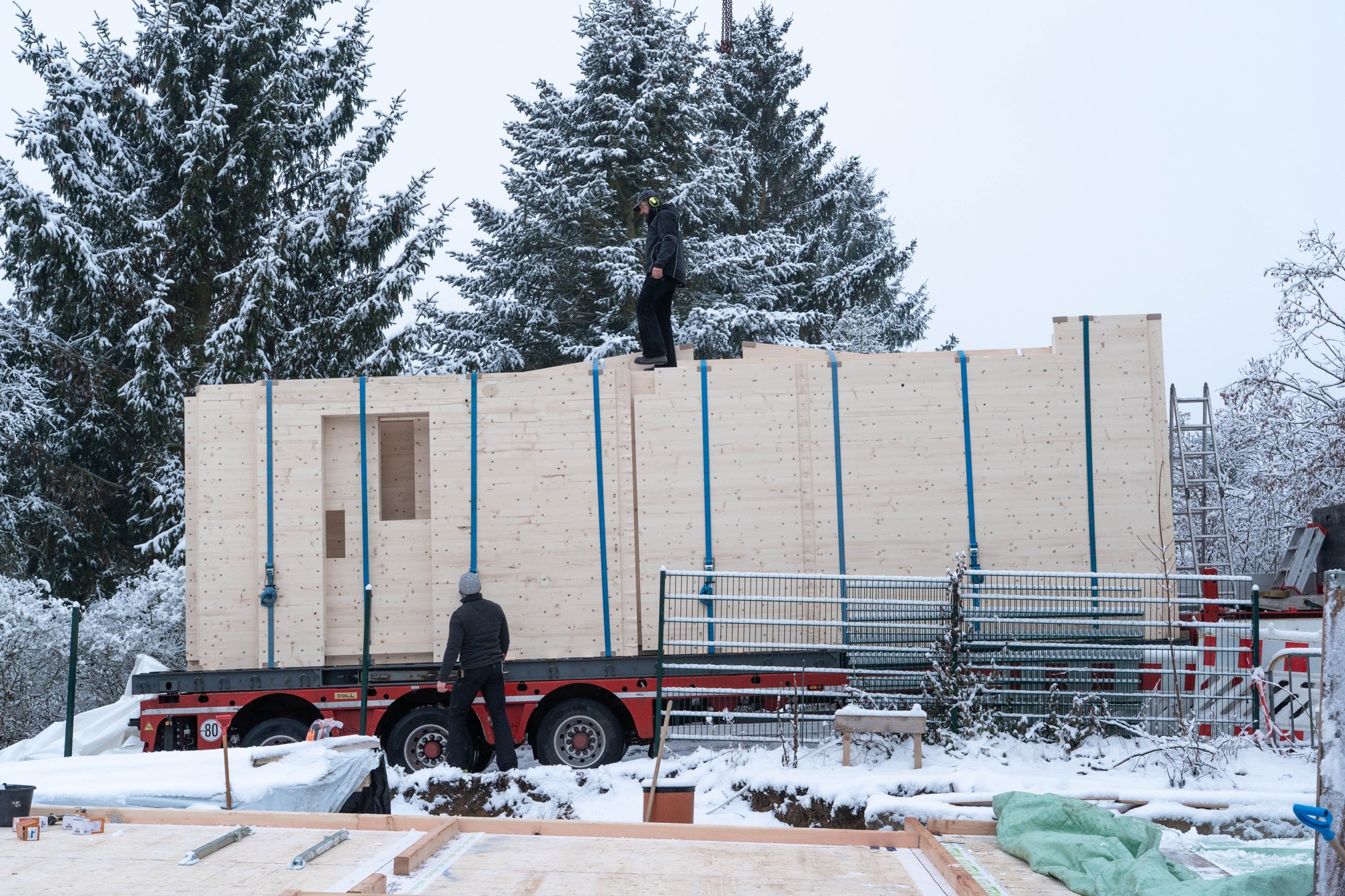 Anlieferung der Holz100-Wandelemente per Tieflader auf einer verschneiten Baustelle