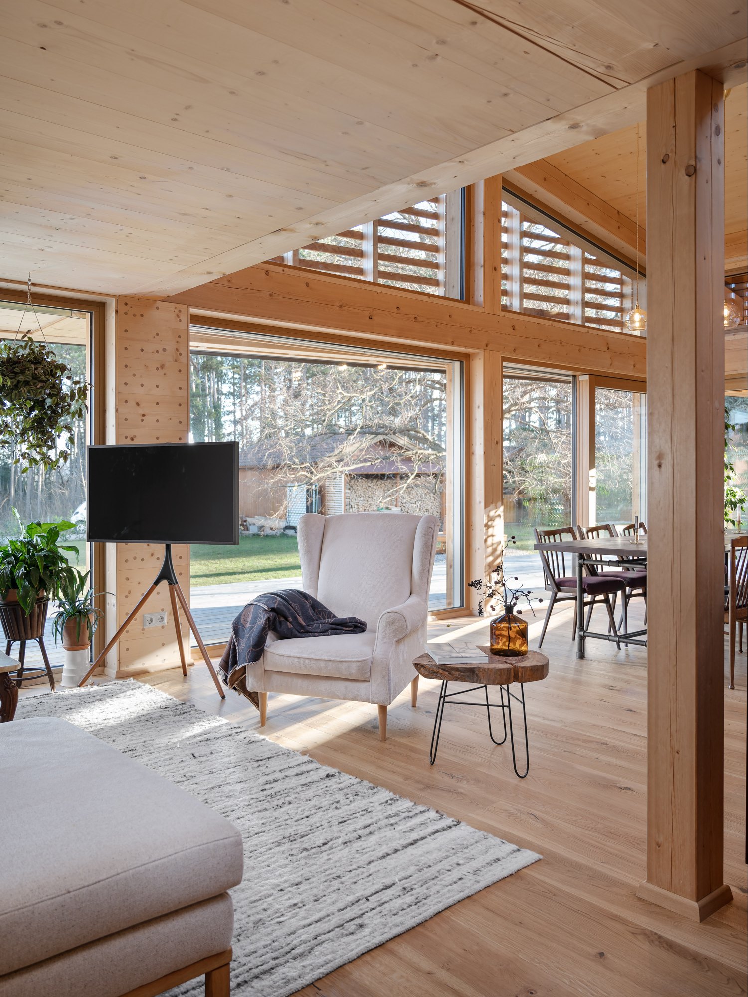 Offener Wohnbereich in Massivholz mit großen Fensterfronten, Sessel und Blick in den Garten